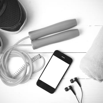 fitness equipment : running shoes,towel,jumping rope and phone on white wood table black and white color tone style