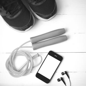 fitness equipment : running shoes,jumping rope and phone on white wood table black and white color tone style