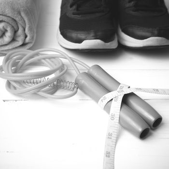 fitness equipment : running shoes,towel,jumping rope and measuring tape on white wood table black and white color tone style