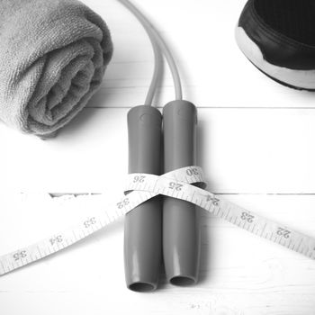 fitness equipment : running shoes,towel,jumping rope and measuring tape on white wood table black and white color tone style