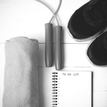 fitness equipment : running shoes,towel,jumping rope and notebook write to do list on white wood table black and white color tone style