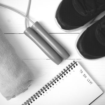 fitness equipment : running shoes,towel,jumping rope and notebook write to do list on white wood table black and white color tone style