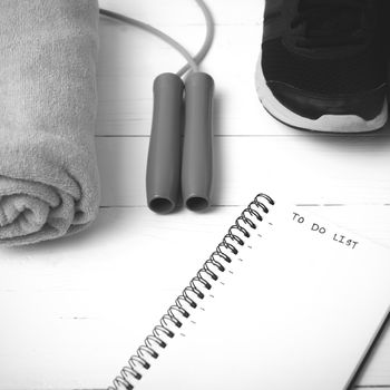 fitness equipment : running shoes,towel,jumping rope and notebook write to do list on white wood table black and white color tone style