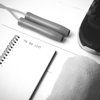 fitness equipment : running shoes,towel,jumping rope and notebook write to do list on white wood table black and white color tone style