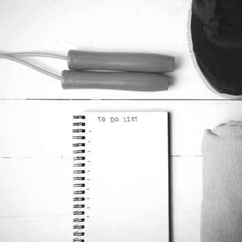 fitness equipment : running shoes,towel,jumping rope and notebook write to do list on white wood table black and white color tone style