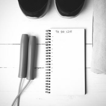 fitness equipment : running shoes,towel,jumping rope and notebook write to do list on white wood table black and white color tone style