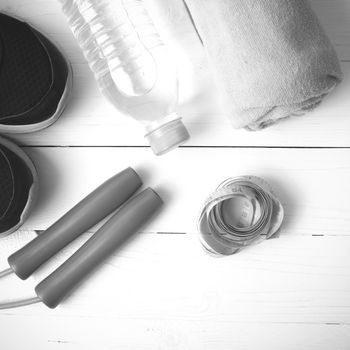 fitness equipment : running shoes,towel,jumping rope,water bottle and measuring tape on white wood table black and white color tone style