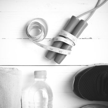 fitness equipment : running shoes,towel,jumping rope,water bottle and measuring tape on white wood table black and white color tone style