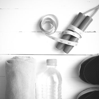 fitness equipment : running shoes,towel,jumping rope,water bottle and measuring tape on white wood table black and white color tone style