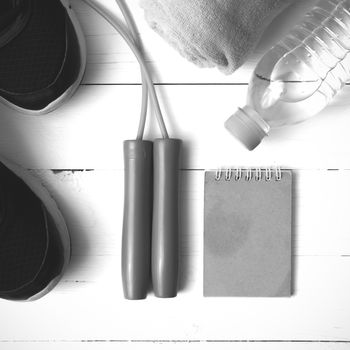 fitness equipment : running shoes,towel,jumping rope,water bottle and notepad on white wood table black and white color tone style