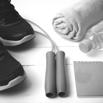 fitness equipment : running shoes,towel,jumping rope,water bottle and notepad on white wood table black and white color tone style