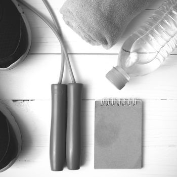 fitness equipment : running shoes,towel,jumping rope,water bottle and notepad on white wood table black and white color tone style