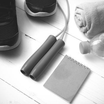 fitness equipment : running shoes,towel,jumping rope,water bottle and notepad on white wood table black and white color tone style