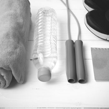 fitness equipment : running shoes,towel,jumping rope,water bottle and notepad on white wood table black and white color tone style