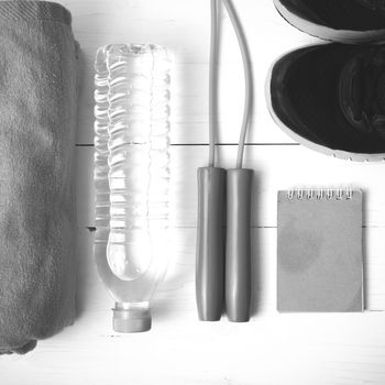 fitness equipment : running shoes,towel,jumping rope,water bottle and notepad on white wood table black and white color tone style