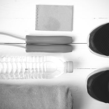 fitness equipment : running shoes,towel,jumping rope,water bottle and notepad on white wood table black and white color tone style