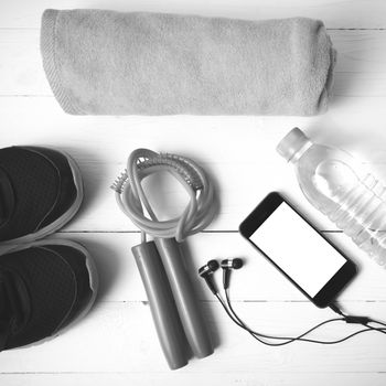 fitness equipment : running shoes,towel,jumping rope,water bottle and phone on white wood table black and white color tone style