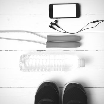 fitness equipment : running shoes,jumping rope,water bottle and phone on white wood table black and white color tone style