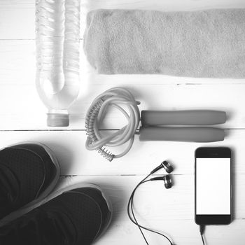 fitness equipment : running shoes,towel,jumping rope,water bottle and phone on white wood table black and white color tone style