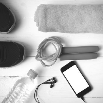 fitness equipment : running shoes,towel,jumping rope,water bottle and phone on white wood table black and white color tone style