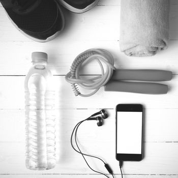 fitness equipment : running shoes,towel,jumping rope,water bottle and phone on white wood table black and white color tone style