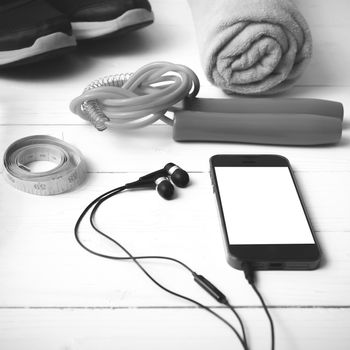 fitness equipment : running shoes,towel,jumping rope,phone and measuring tape on white wood table black and white color tone style