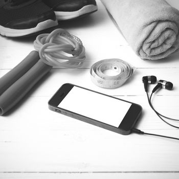 fitness equipment : running shoes,towel,jumping rope,water bottle,phone and measuring tape on white wood table black and white color tone style