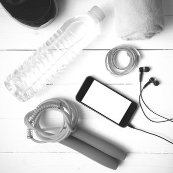 fitness equipment : running shoes,towel,jumping rope,water bottle,phone and measuring tape on white wood table black and white color tone style