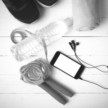 fitness equipment : running shoes,towel,jumping rope,water bottle,phone and measuring tape on white wood table black and white color tone style