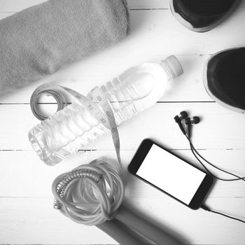 fitness equipment : running shoes,towel,jumping rope,water bottle,phone and measuring tape on white wood table black and white color tone style