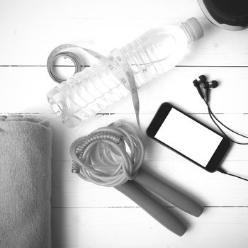 fitness equipment : running shoes,towel,jumping rope,water bottle,phone and measuring tape on white wood table black and white color tone style