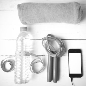 fitness equipment :towel,jumping rope,water bottle,phone and measuring tape on white wood table black and white color tone style