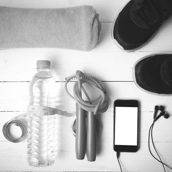 fitness equipment : running shoes,towel,jumping rope,water bottle,phone and measuring tape on white wood table black and white color tone style