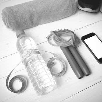 fitness equipment : running shoes,towel,jumping rope,water bottle,phone and measuring tape on white wood table black and white color tone style