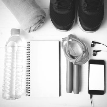 fitness equipment : running shoes,towel,jumping rope,water bottle,phone and notepad on white wood table black and white color tone style