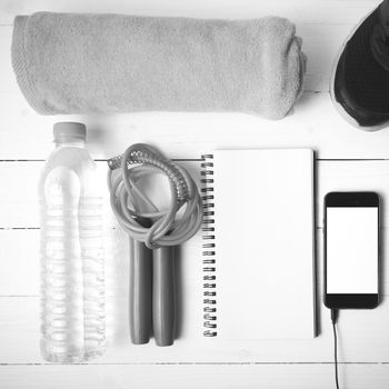 fitness equipment : running shoes,towel,jumping rope,water bottle,phone and notepad on white wood table black and white color tone style