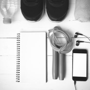 fitness equipment : running shoes,towel,jumping rope,water bottle,phone and notepad on white wood table black and white color tone style