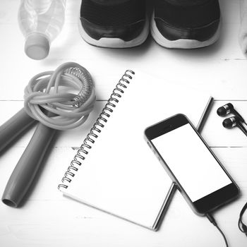 fitness equipment : running shoes,towel,jumping rope,water bottle,phone and notepad on white wood table black and white color tone style