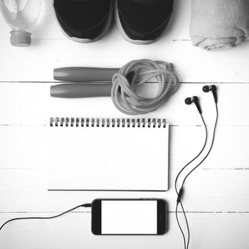 fitness equipment : running shoes,towel,jumping rope,water bottle,phone and notepad on white wood table black and white color tone style