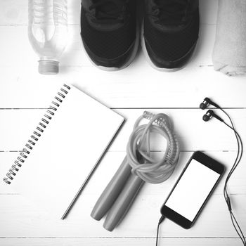 fitness equipment : running shoes,towel,jumping rope,water bottle,phone and notepad on white wood table black and white color tone style