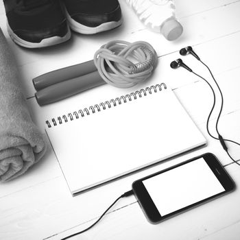 fitness equipment : running shoes,towel,jumping rope,water bottle,phone and notepad on white wood table black and white color tone style