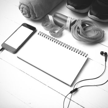 fitness equipment : running shoes,towel,jumping rope,phone,notepad and measuring tape on white wood table black and white color tone style