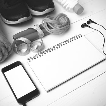 fitness equipment : running shoes,towel,jumping rope,water bottle,phone,notepad and measuring tape on white wood table black and white color tone style