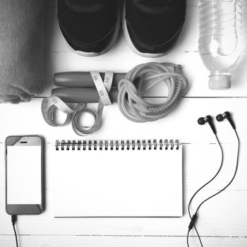 fitness equipment : running shoes,towel,jumping rope,water bottle,phone,notepad and measuring tape on white wood table black and white color tone style