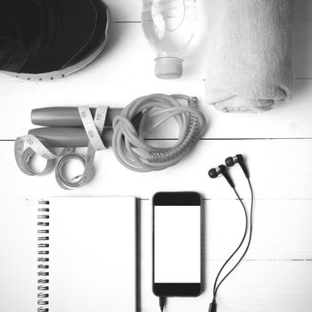 fitness equipment : running shoes,towel,jumping rope,water bottle,phone,notepad and measuring tape on white wood table black and white color tone style