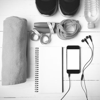 fitness equipment : running shoes,towel,jumping rope,water bottle,phone,notepad and measuring tape on white wood table black and white color tone style