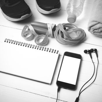 fitness equipment : running shoes,towel,jumping rope,water bottle,phone,notepad and measuring tape on white wood table black and white color tone style