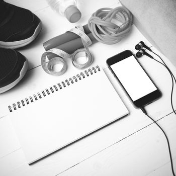 fitness equipment : running shoes,towel,jumping rope,water bottle,phone,notepad and measuring tape on white wood table black and white color tone style