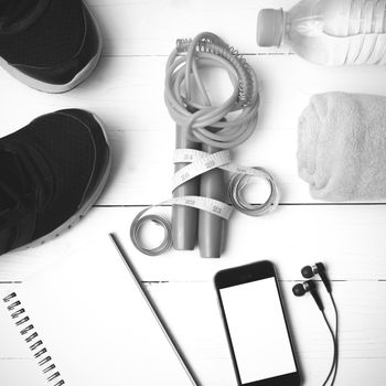 fitness equipment : running shoes,towel,jumping rope,water bottle,phone,notepad and measuring tape on white wood table black and white color tone style