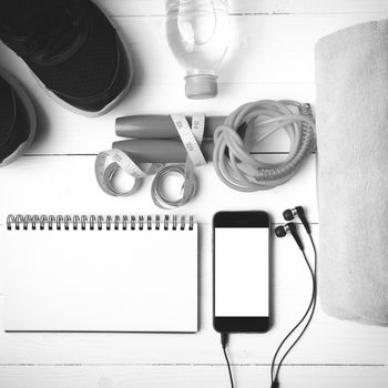 fitness equipment : running shoes,towel,jumping rope,water bottle,phone,notepad and measuring tape on white wood table black and white color tone style